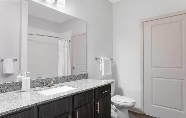 A bathroom with a sink, mirror, toilet and a white door.