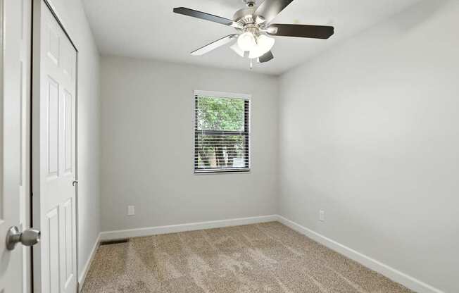 A room with a ceiling fan and a window with blinds.