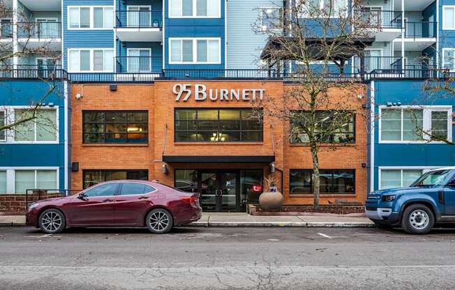 A red car is parked in front of a building with the sign 95 Burnett.