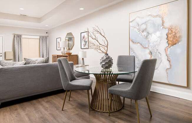 A modern dining room with a glass table and grey chairs.