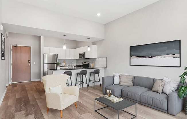 Model Living Room with Wood-Style Flooring and View of Kitchen at Seven Skies Apartments located in Sandy, UT.