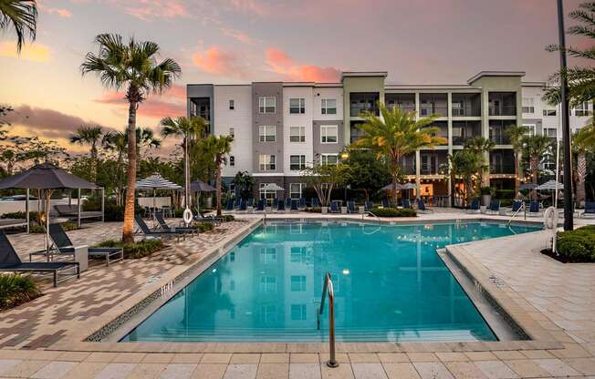 a swimming pool in front of an apartment building at sunset