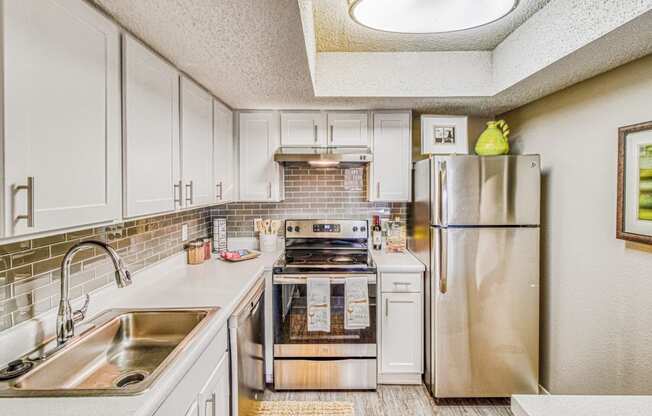 Model home renovated kitchen with stainless steel appliances and white cabinets at Hillside Creek Apartments in Austin, TX