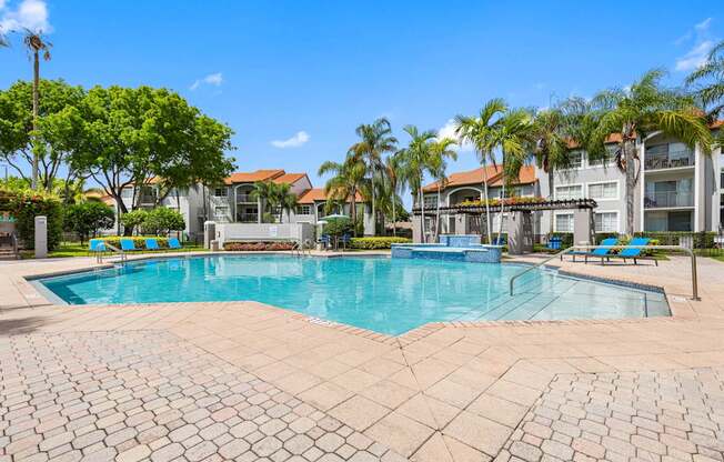 A large swimming pool surrounded by a brick patio and palm trees.