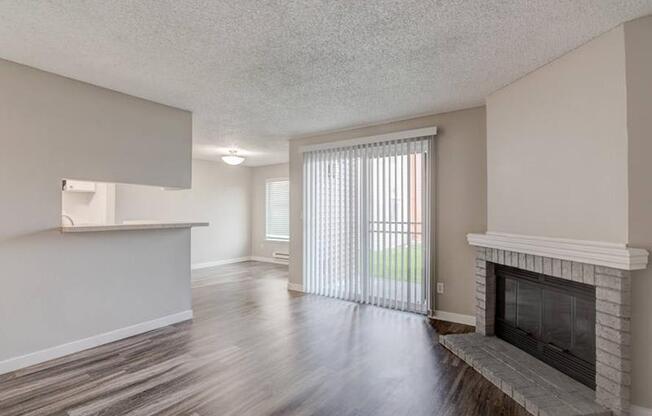 A living room with a fireplace, sliding glass doors to a patio, a kitchen breakfast bar, and a dining room to the left.