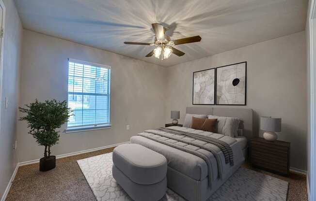 A bedroom with a large bed, a ceiling fan, and a potted plant.