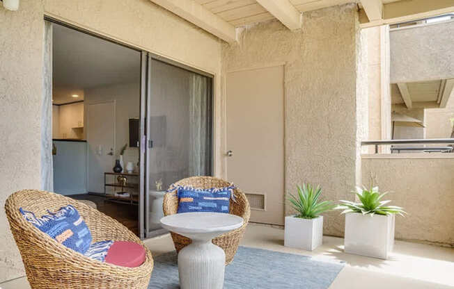 A wicker chair with a blue cushion sits in a sunny room with a table and potted plants.