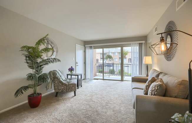 Mechanicsburg Apartments | Delbrook Manor Apartments | a living room with a couch chair and a potted plant in front of a sliding glass