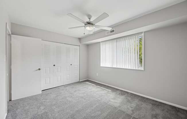 A room with a ceiling fan and a window with blinds.