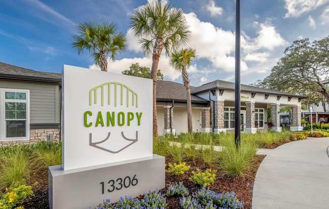 A sign for Canopy with a house in the background.