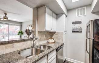 A kitchen with a stainless steel refrigerator and a granite countertop.