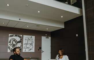 a man and a woman sitting in a lobby with their laptops