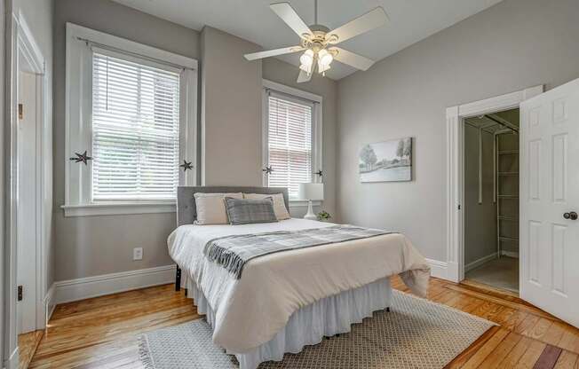 A bedroom with a bed, pillows, a ceiling fan, and a window with blinds.
