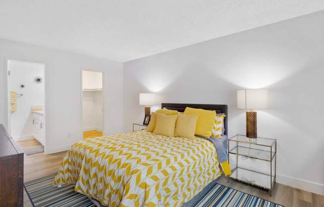 A bedroom with a bed covered in yellow and white bedding at Verandas Apartments, West Covina, California