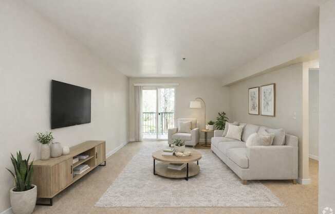 A living room with a white couch, a coffee table, and a flat-screen TV mounted on the wall.
