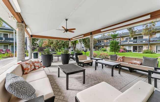 A patio with a white couch, black and white pillows, and a ceiling fan.