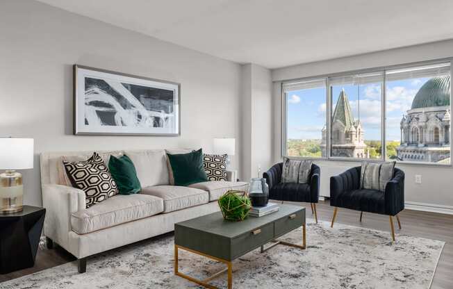 a living room with a beige couch and two black and white chairs and a large window