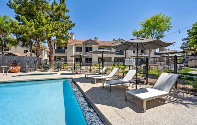 A pool area with sun loungers and umbrellas in front of a building.