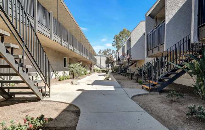 A concrete pathway leads between apartment buildings with metal staircases on either side.