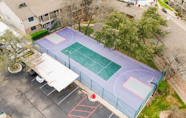 an aerial view of a tennis court and a basketball court with trees and a house