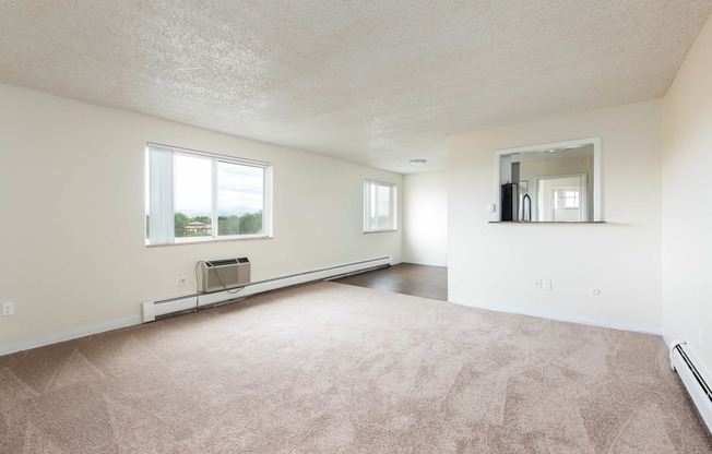 the living room and dining room of an apartment with carpeting and a large window