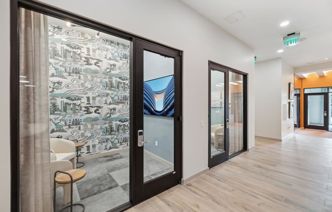 a corridor with glass doors and a lobby with chairs and a table