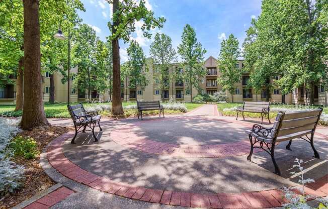a courtyard with benches and trees with an apartment building in the background