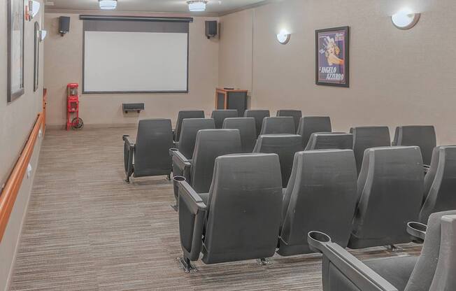 A movie theater with rows of grey seats and a white screen.