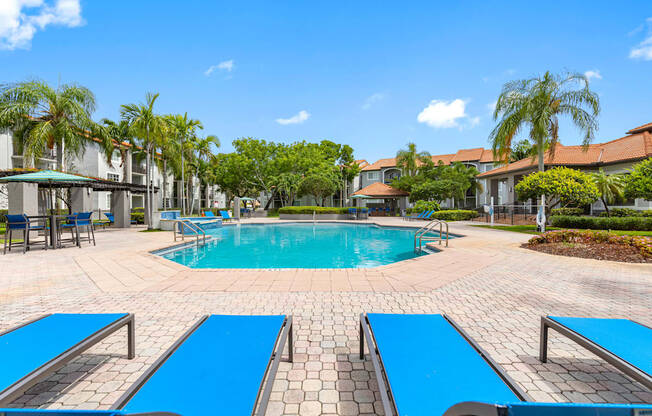 A swimming pool surrounded by blue lounge chairs and palm trees.