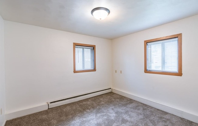 a bedroom of a house with carpet and two windows. Fargo, ND Spring Apartments