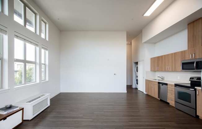 an empty living room with white walls and wood floors and a kitchen with wood cabinets