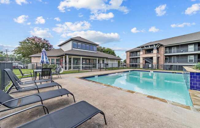 A pool area with lounge chairs and a building in the background.