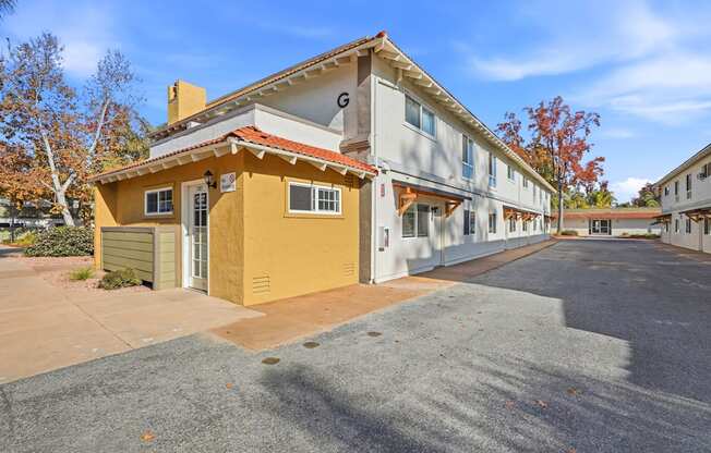 A yellow house with a red roof is in front of a white building.