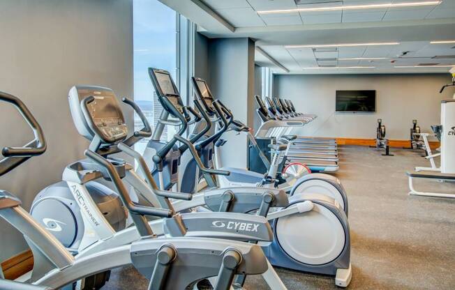 A gym with a row of stationary bikes and a television mounted on the wall.