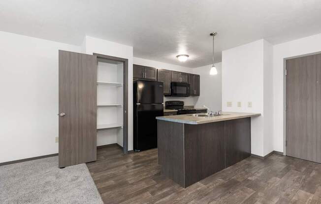 A kitchen with a black fridge and microwave, brown cabinets, and a grey rug.