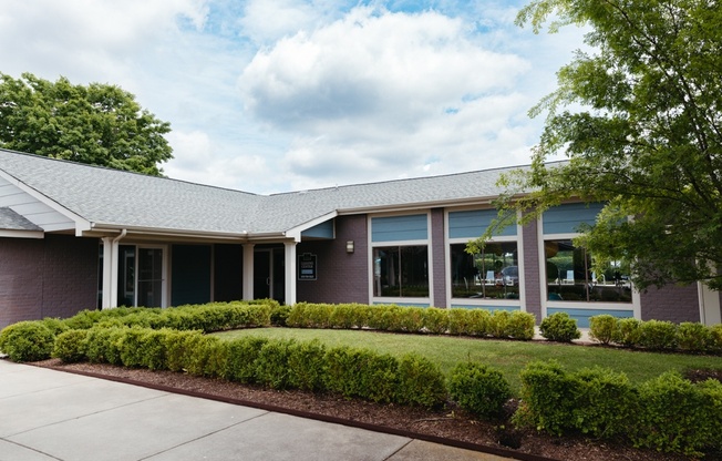 the front of a brick building with a sidewalk and landscaping