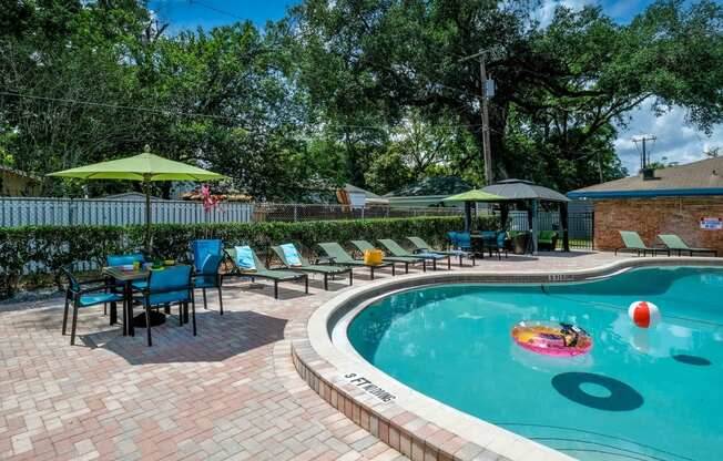 Poolside view of Community pool at Watermarc Apartments in Lakeland, FL with green lounge chairs and patio tables with sun umbrellas.