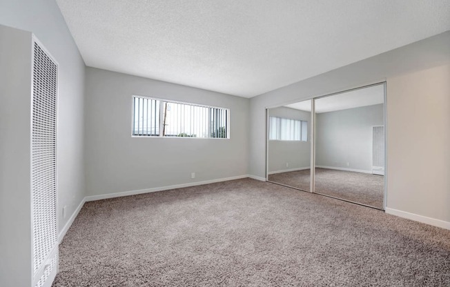 an empty living room with a mirrored closet and carpet at Sunset Square, West Covina, CA