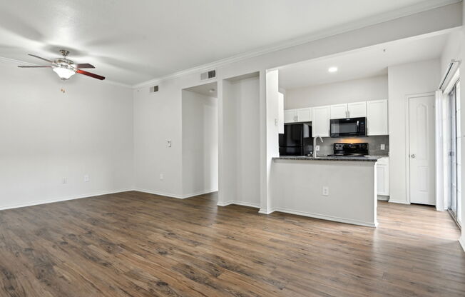 A room with a ceiling fan and a kitchen area with a microwave, oven, and refrigerator.