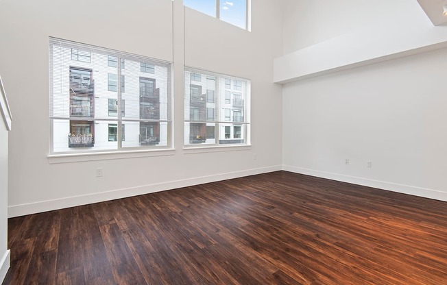 A room with wooden floors and windows showing a view of a building outside.