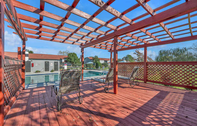 A red wooden pergola with a pool table and chairs underneath it.