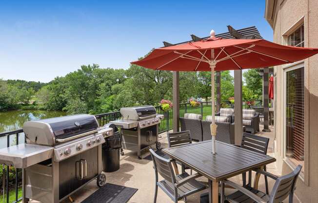 a patio with barbecue grills and tables with umbrellas