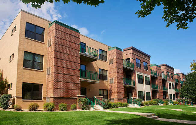 A large brick apartment building with balconies and a green lawn in front.