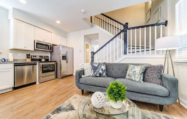 A modern kitchen with a grey couch and a glass coffee table.