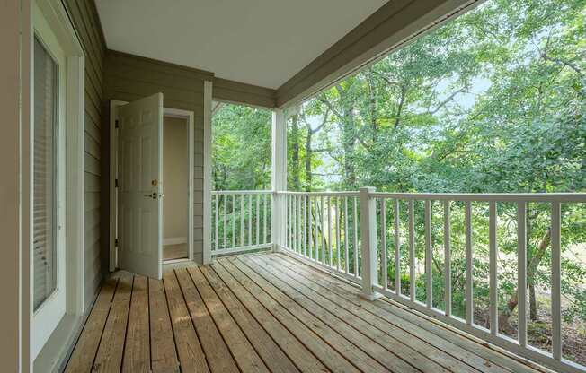A wooden deck with a white railing and a door leading to a lush green forest.