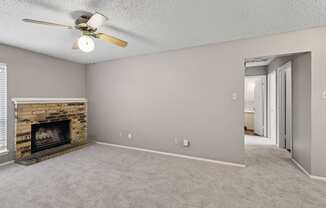 A living room with a fireplace, carpeted floor, and a ceiling fan at Heritage Square Apartments in Waco, TX