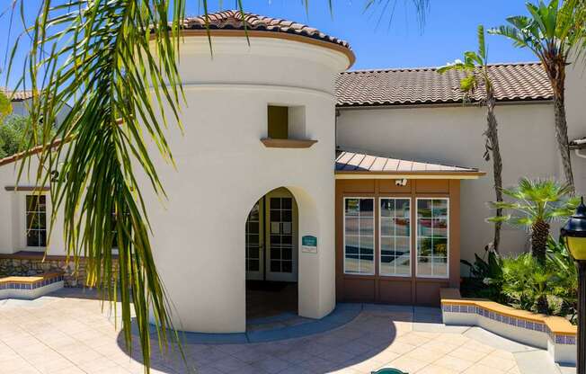 A building with a white facade and a brown roof is surrounded by greenery.