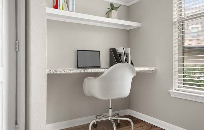 A white chair is in front of a desk with a laptop and a plant on it.