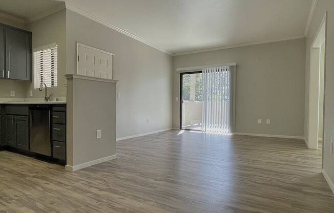 an empty living room with a kitchen and a sliding glass door
