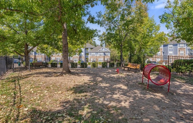 A playground with a red slide and a tree in the middle of a dirt area.